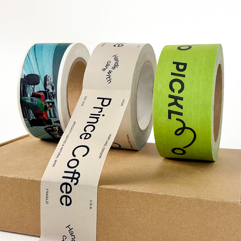 Three rolls of paper packing tape with printed labels on a cardboard surface