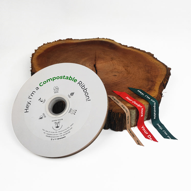 A roll of custom compostable ribbon with a logo printed on it, displayed next to a wooden object for a natural appearance.